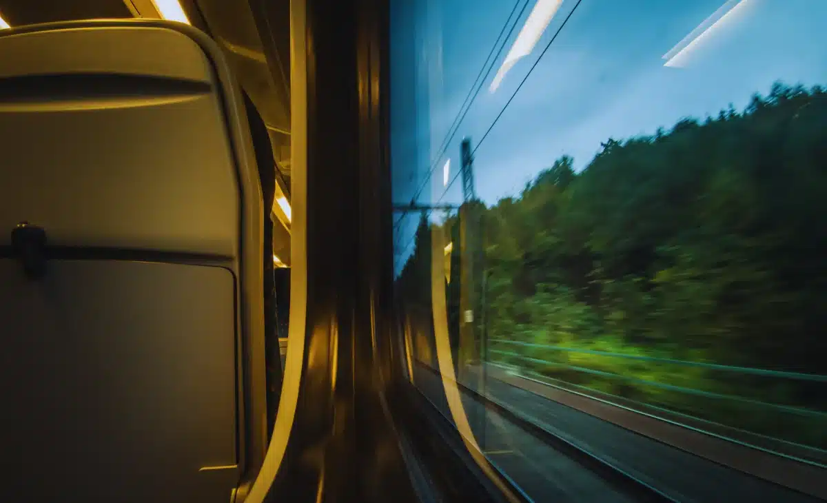 View from inside a moving train looking out at railway tracks and green landscape.